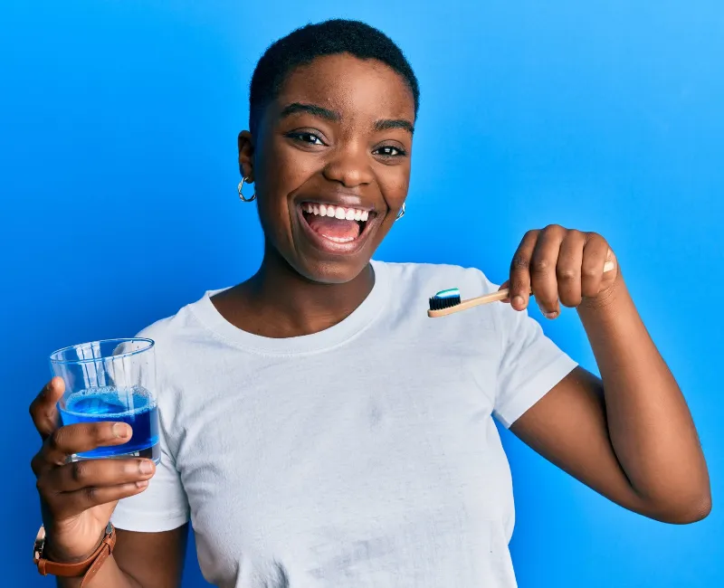 Woman holding glass of mouthwash and toothbrush