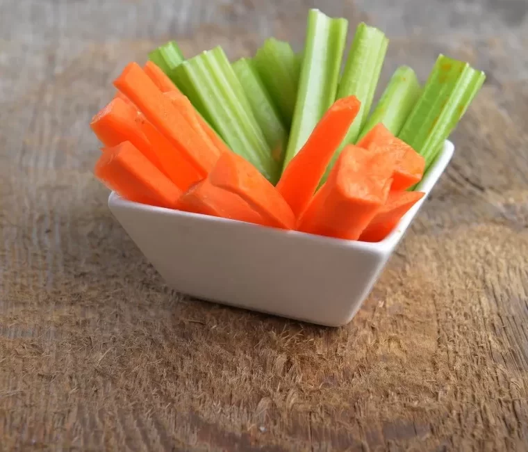 Bowl of carrot and celery sticks on wooden background
