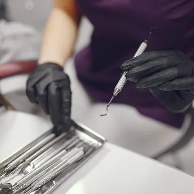 Dentist wearing black gloves selecting a dental scaler from a tray of instruments