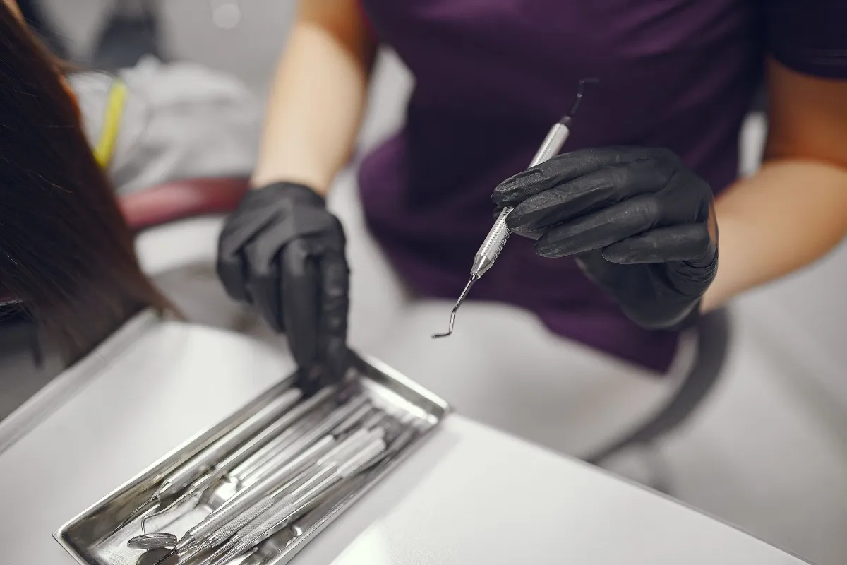 Dentist wearing black gloves selecting a dental scaler from a tray of instruments