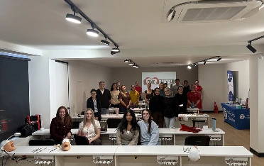 Group of people posing for a photo in a training lab with workstations and mannequin heads in front.